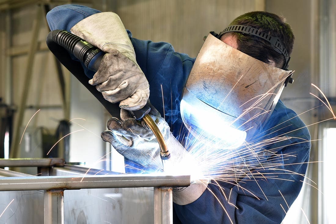 Welder in protective gear welding metal with bright sparks
