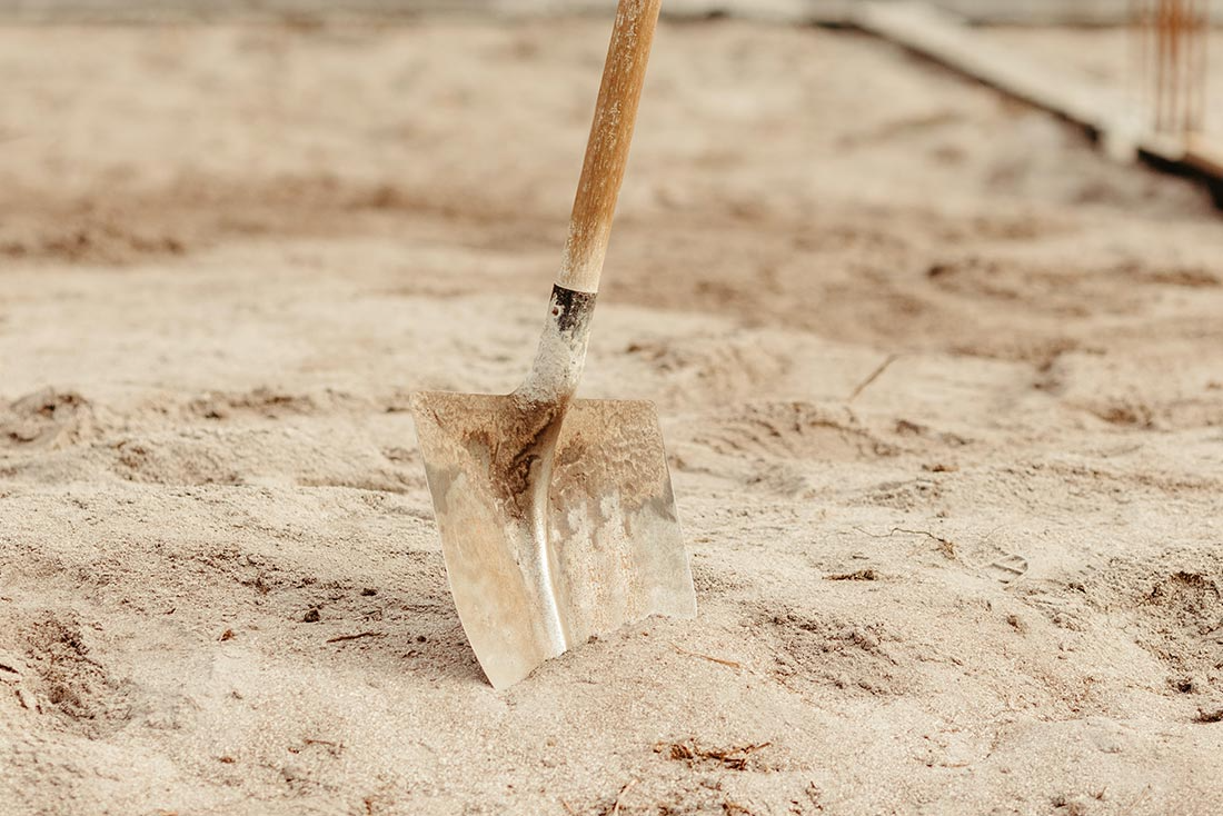 Metal shovel with wooden handle upright in sandy ground
