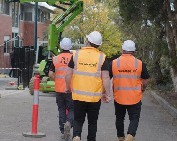 Three workers in safety vests and helmets walk on site road